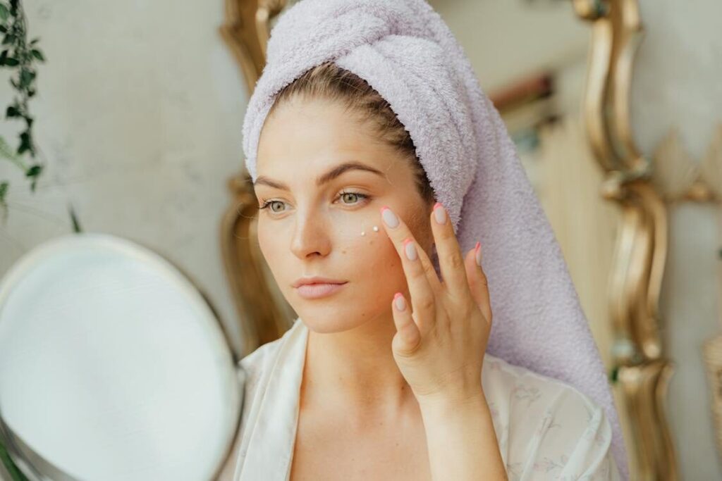 A woman applies moisturizer to her face.