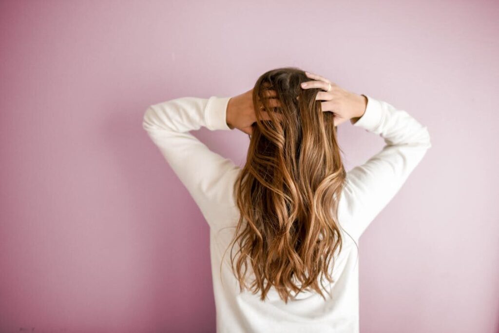 A female standing with their back to the camera, running their fingers through their long hair.