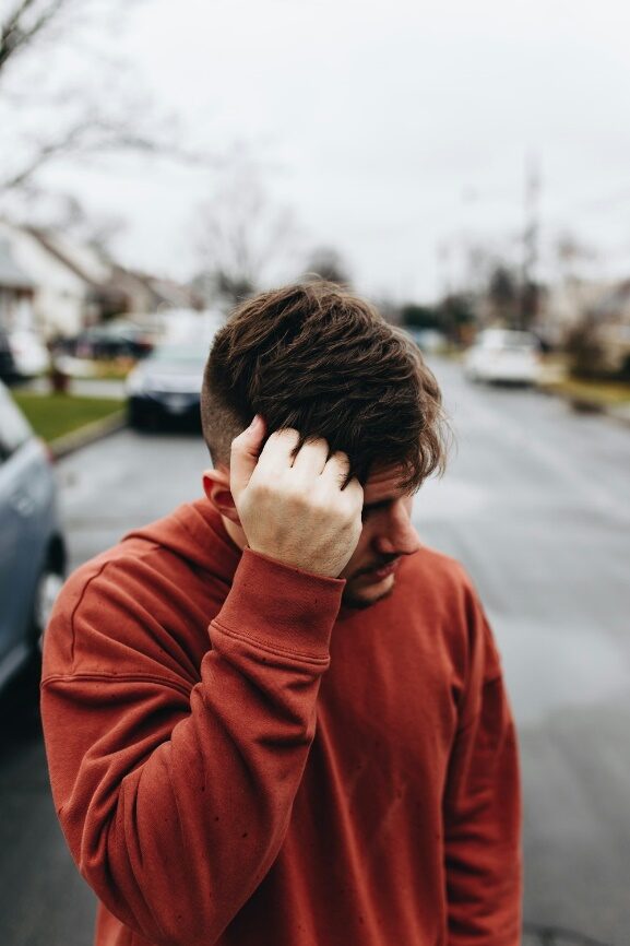 A man dressed in a red sweatshirt, running his hand through his hair.