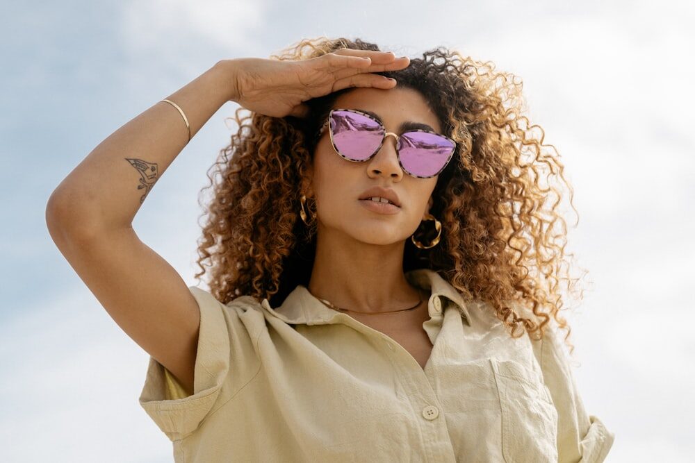  A Woman Wearing Shades and Papaya Skincare Products Shields Her Face Under a Clear, Blue Sky